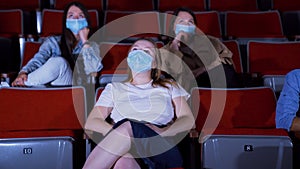 Young women in masks watch movie at cinema. Media. Watching movies in cinemas in context of coronavirus pandemic. People