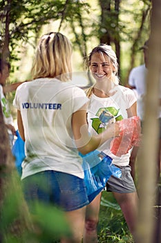 Young women picking trash in nature. Group of young friends in forest volunteering. Ecology, environmentalism, green living,