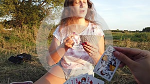 Young women are playing cards in nature. Two women are sitting on the grass and gambling in summer.