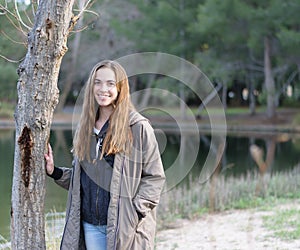 Young women poses outdoors next to a tree and lake