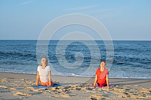 Young women practicing yoga on the beach. Beautiful girls practicing yoga Cobra exercise