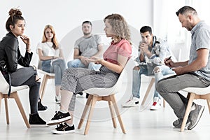 Young woman resolving problem with rebellious friend during group therapy with counselor