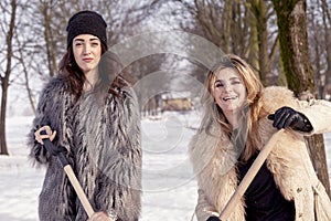 Young women shoveling snow near a small wood