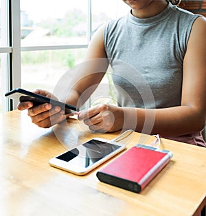 Young women sitting on the chair playing with smartphone While charging the smartphone battery and device Charge Sharing