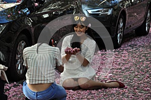 Young women sitting on road covered with red rose cherry blossoms