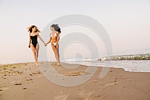 Young women smiling and holding hands while running on beac