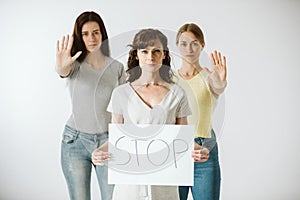 Young women are standing next to each other, one of them holding a piece of paper with the word stop