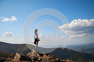 Young women standing on rock on top of the mountain. Feeling happy and free. Natural landscape in summer. Sunny rural scenery.