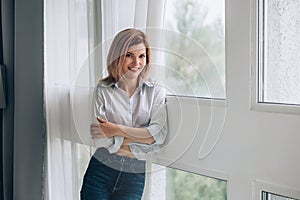 A young woman stands by the panoramic window and smiles at the camera.