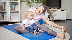 Young woman stretching and doing fitness with her little baby boy at home. Concept of healthcare, sports, childcare and kids