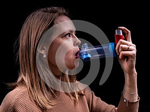 Young women taking asthma medication with an inhaler and spacer with a black background