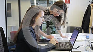 Young women talking while looking at laptop in modern office.