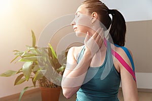 Young women touching her neck with hand and elastic kinesio tape on her shoulder. Performing exercise at home. Kinesiology