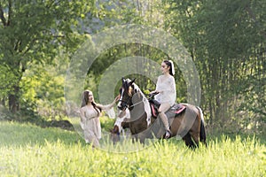 Young woman in white dress with horse. Beautiful woman riding a horse at sunset on the forest. Young beauty girl with a horse in