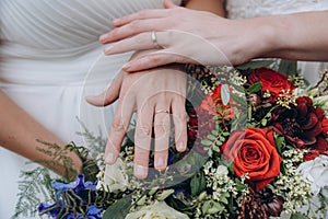 Young women in white dresses suit showing wedding rings with bouquet of red flowers