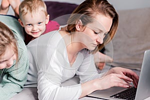 Young women works at home with laptop along with two children.Children want to communicate with mother, make noise and interfere