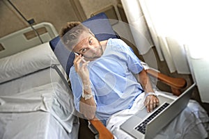 Young workaholic business man in hospital room sick and injured after accident working with mobile phone and computer laptop photo