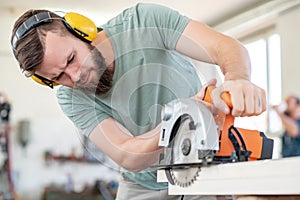 Young worker in a carpenter`s workshop with hand saw