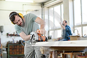 Young worker in a carpenter`s workshop with hand saw