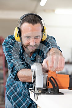 Young worker in a carpenter`s workshop with hand saw