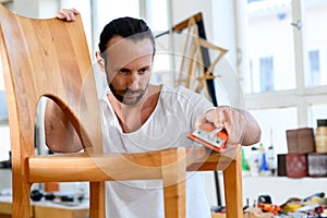 Young worker in a carpenters workshop with wooden chair photo