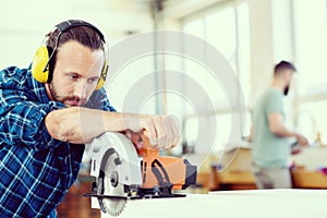 Young worker in a carpenters workshop with hand saw