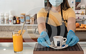 Young worker delivering cup of coffee inside restaurant while wearing safety mask - Focus on glass of juice