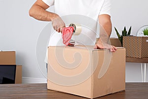 Young worker packing cardboard box in room. Moving service