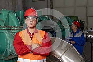 Young Worker in Red Coveralls and Hardhat Standing in Industrial Interior With Pipes and Generators