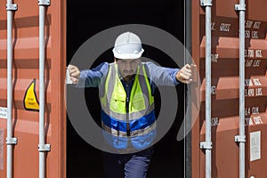 Young worker with safety vest and yellow hardhat pushing container door with both hand, open it from inside