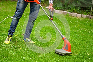 Young worker with a string lawn trimmer mower cutting grass in a blurred nature background