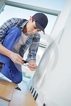 Young worker in uniform installing new baseboard at home