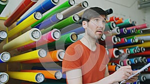 Young worker in warehouse with clipboard checking inventory. Man works in sales department of advertising materials