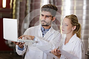 young workers wearing labcoats holding white laptop photo