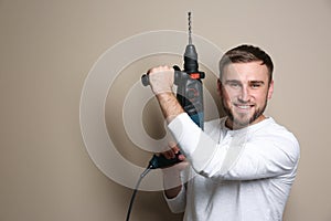 Young working man with rotary hammer on beige background