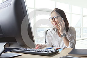 Young working woman talking to phone with watching on computer o