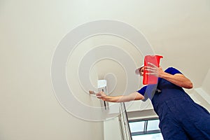 Young workman is painting  the wall with paintbrush