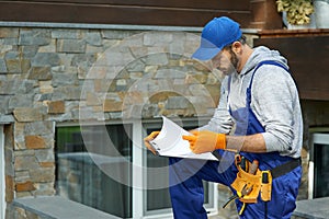 Young workman in uniform looking focused, standing outdoors with papers while working on construction project