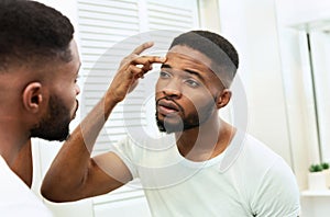 Young worried african man checking his wrinkles