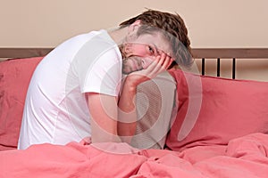 Young worried sick man sitting on bed at home scary and desperate suffering insomnia