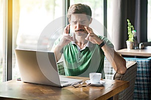 Young worry hopeful businessman in green t-shirt sitting with closed eyes and crossed fingers and hope to win