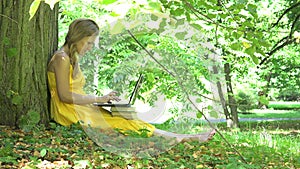 Young writer woman typing laptop keyboard sitting on grass under tree. 4K