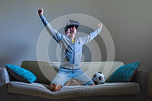 Young xcited gamer man using VR virtual reality goggles headgear playing football simulation game celebrating scoring goal at home