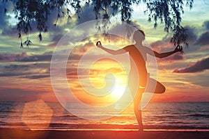 Young yoga girl practicing on the ocean beach at amazing beautiful sunset. Nature.