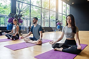 Young yoga practitioners in group doing yoga in modern fitness class indoor