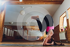 Young yogi attractive woman practicing yoga concept, standing in salamba sirsasana exercise, headstand pose, working out