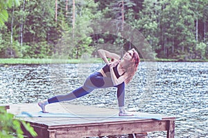 Young yogi  girl  practicing yoga, Parsvakonasana, side angle pose, on the lake.  Concept of healthy life and natural balance