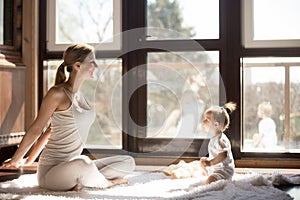 Young yogi mother and baby daughter sitting, healthy sporty day