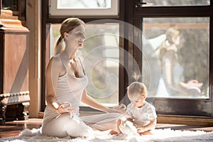 Young yogi mother in Easy Seat pose, baby daughter near