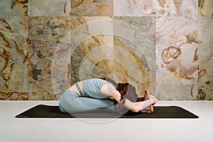 Young yogini practicing Janusirsasana pose in pastel blue leggins and top